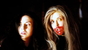 Brigette (Emily Perkins) and Ginger (Katharine Isabelle), bottom half of her face coated in blood, are on guard in GINGER SNAPS 2: UNLEASHED