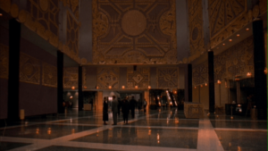 A small crowd gathers in what looks to be a dimly-lit lobby...patterned similarly to the puzzle box in Hellraiser III